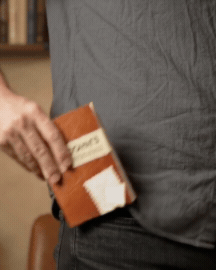 Man placing a John's pocket puzzle book into the front pocket of his pants. 