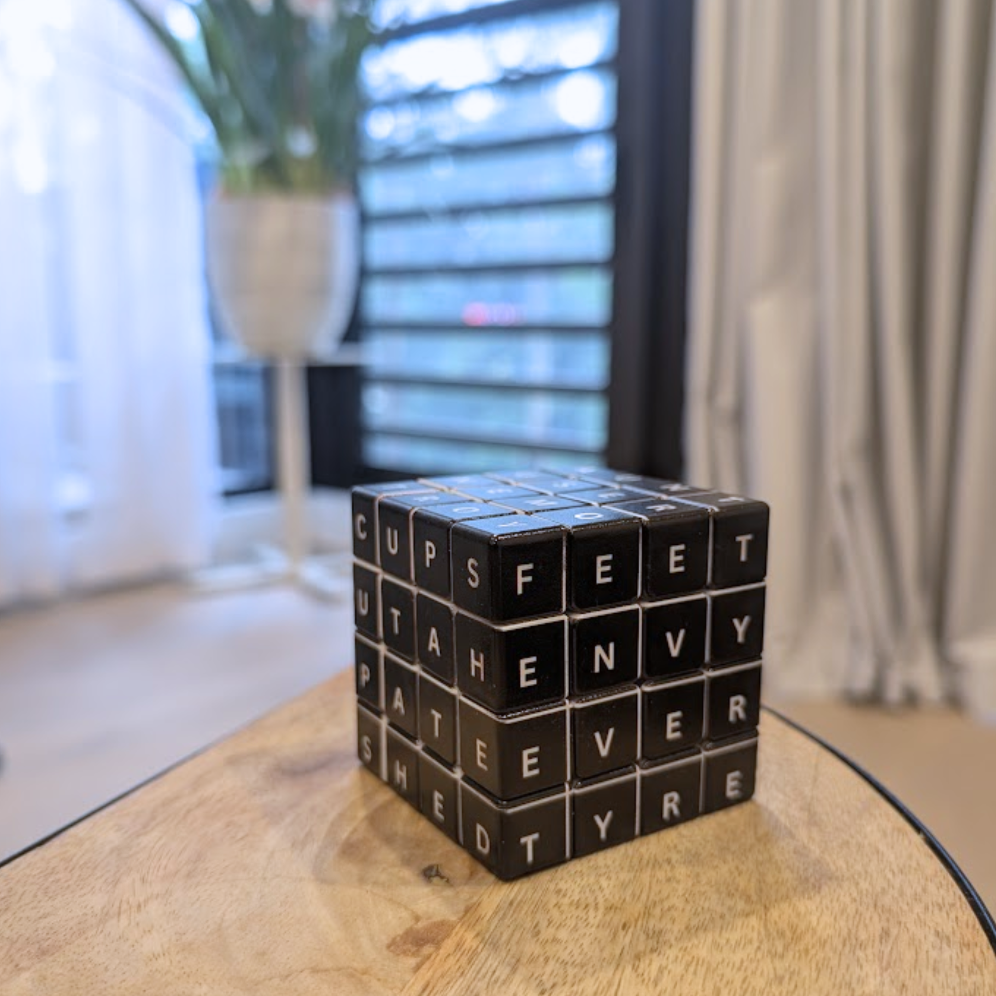 "Witty Word Cube on a wooden table, featuring a 4x4x4 rotating 3D letter grid where each side is used to spell out different words.