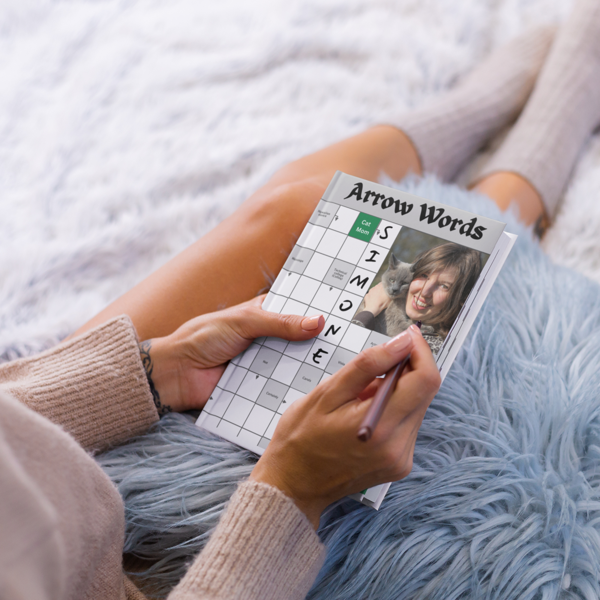 A person relaxing on a bed while solving a personalized Arrow Words puzzle book.
