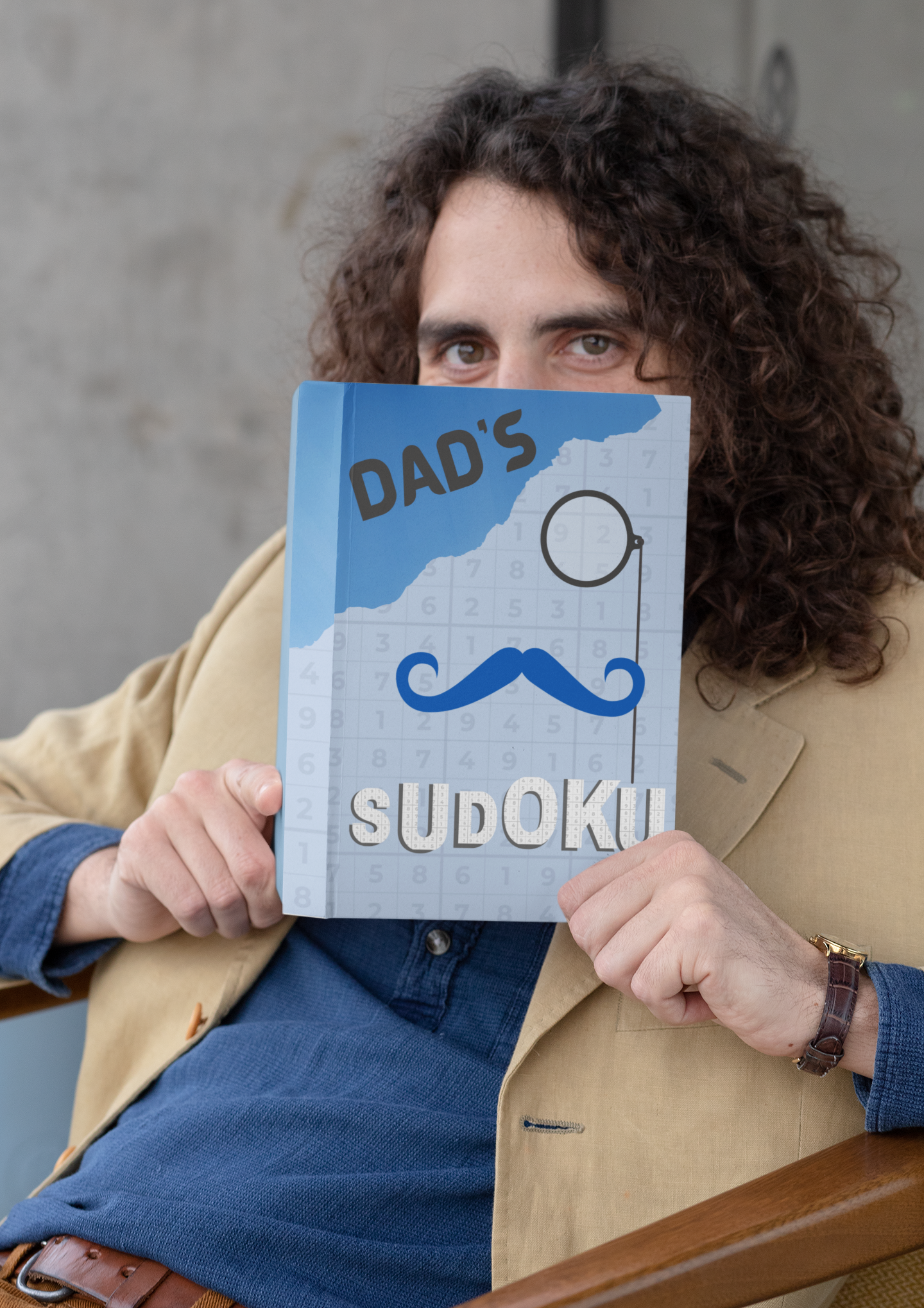 Man holding a blue book titled 'Dad's sudoku'