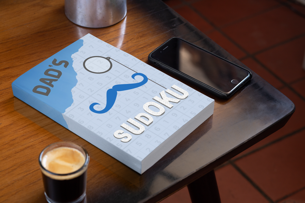 A lifestyle photo of Dad's Sudoku book on a coffee table next to a phone and expresso coffee