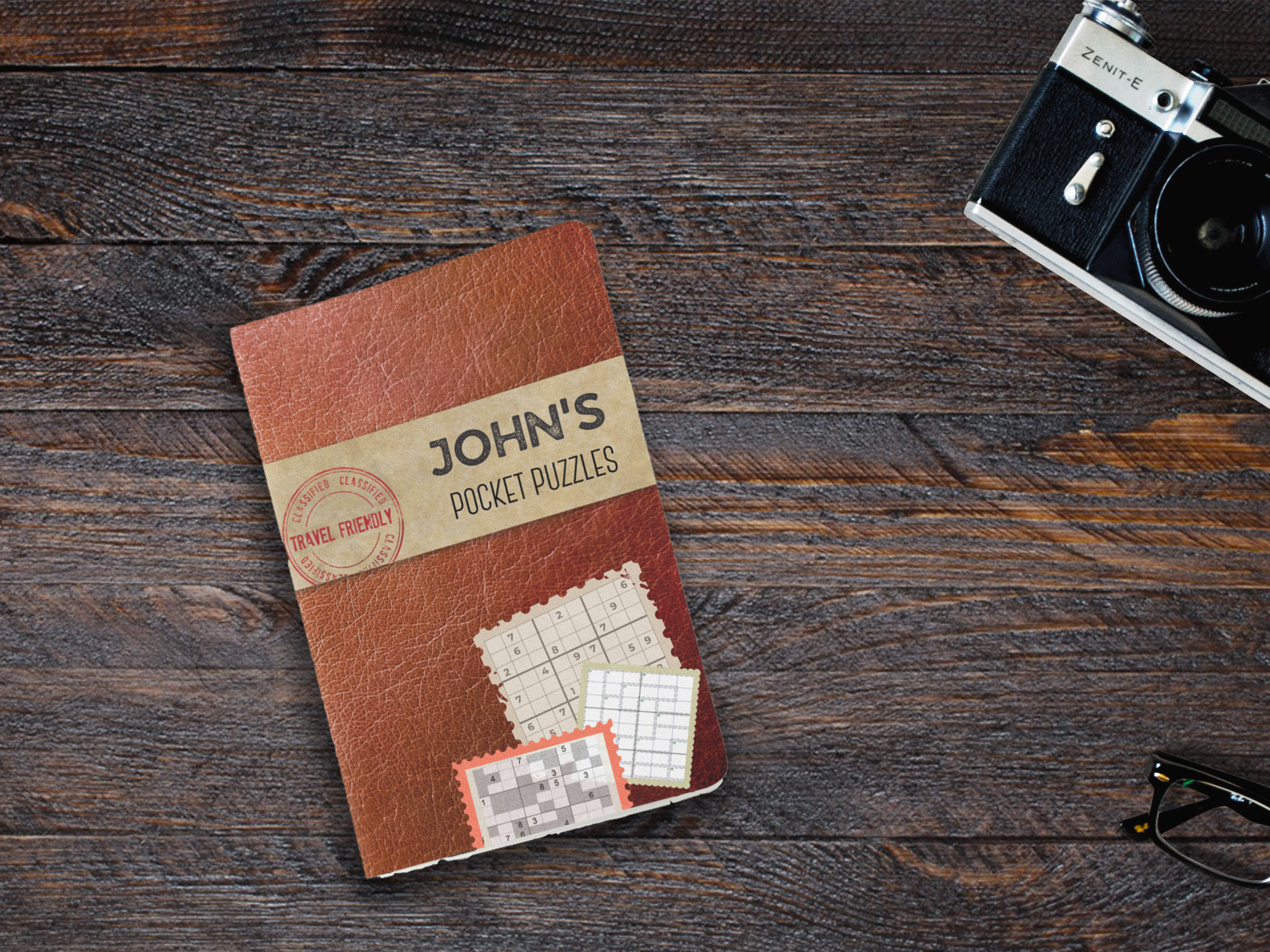 Custom brown leather-look travel puzzle book; a personalized pocket-sized Sudoku gift featuring a smooth  finish and 'Travel Friendly' stamp design on dark wooden surface.