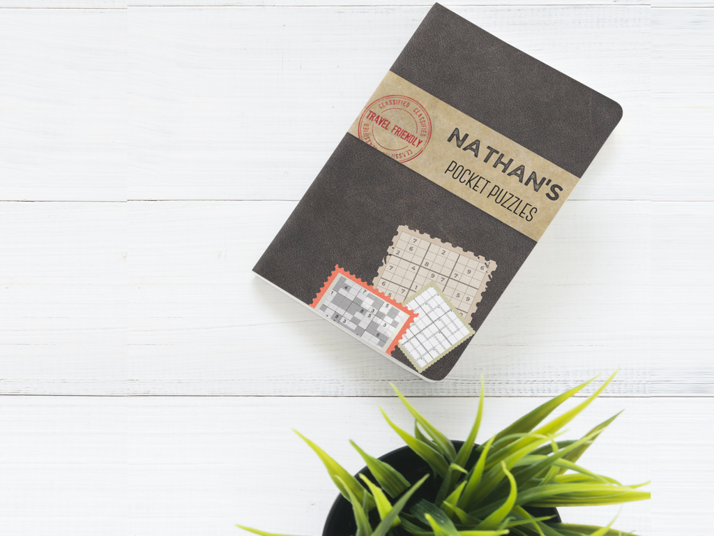 Personalized 'Nathan’s Pocket Puzzles' in the Matte Black cover style, shown on a white wood surface with a green plant for a clean, modern look.