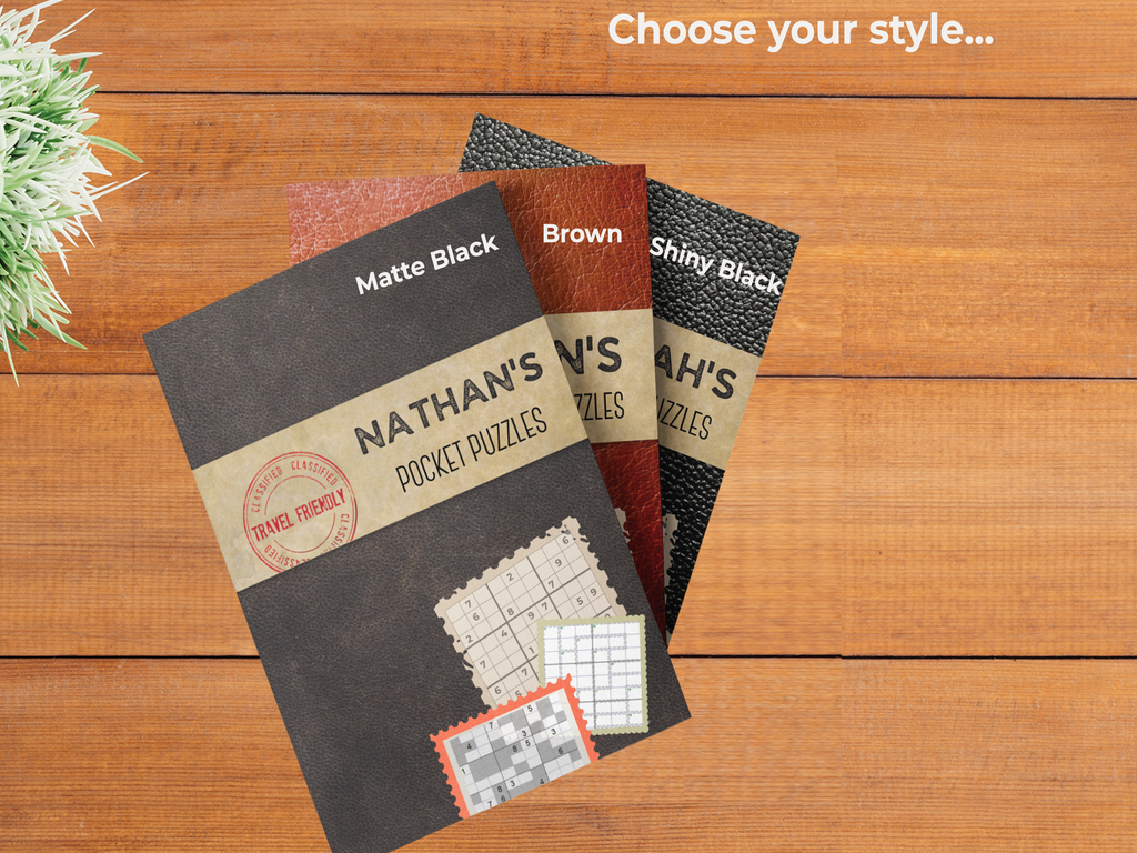 A selection of three personalized Pocket Puzzle books in Matte Black, Brown leather-style, and Shiny Black finishes, displayed on a wooden surface with the text 'Choose your style...