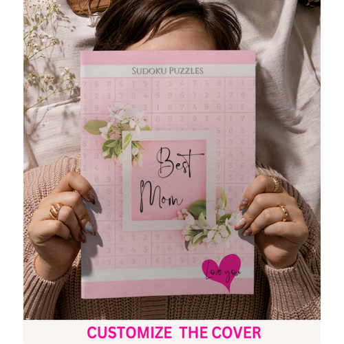A person holding a pink sudoku puzzle book with 'Best Mom' text and a heart symbol on the cover, indicating it's a customizable gift item.